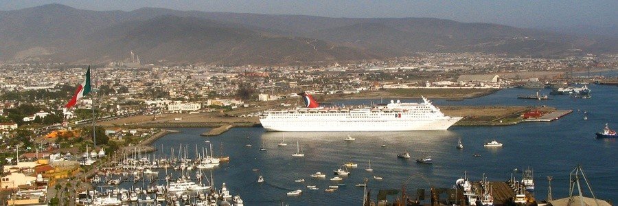 Ensenada beaches near the cruise port with a large cruise ship docked in the harbor, surrounded by smaller boats, marina views, and the coastal city with mountains in the background in Baja California Mexico