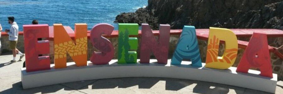 Colorful Ensenada sign overlooking the Pacific Ocean with rocky coastal cliffs and deep blue water in Baja California, capturing a popular photo spot near Ensenada beaches with scenic ocean views and bright decorative letters representing the city