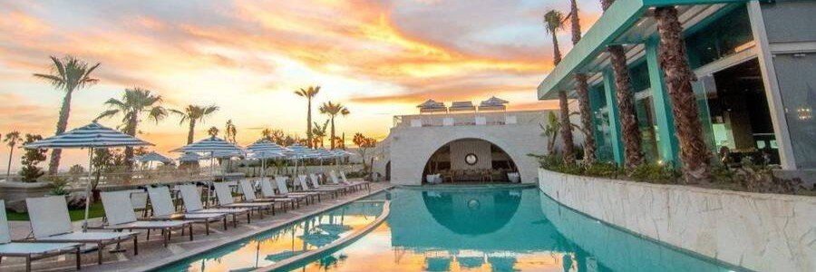 Ensenada beaches near Torre Lucerna Hotel with a modern pool reflecting a colorful sunset sky, surrounded by palm trees, lounge chairs, and contemporary architecture overlooking the Pacific Ocean in Baja California Mexico