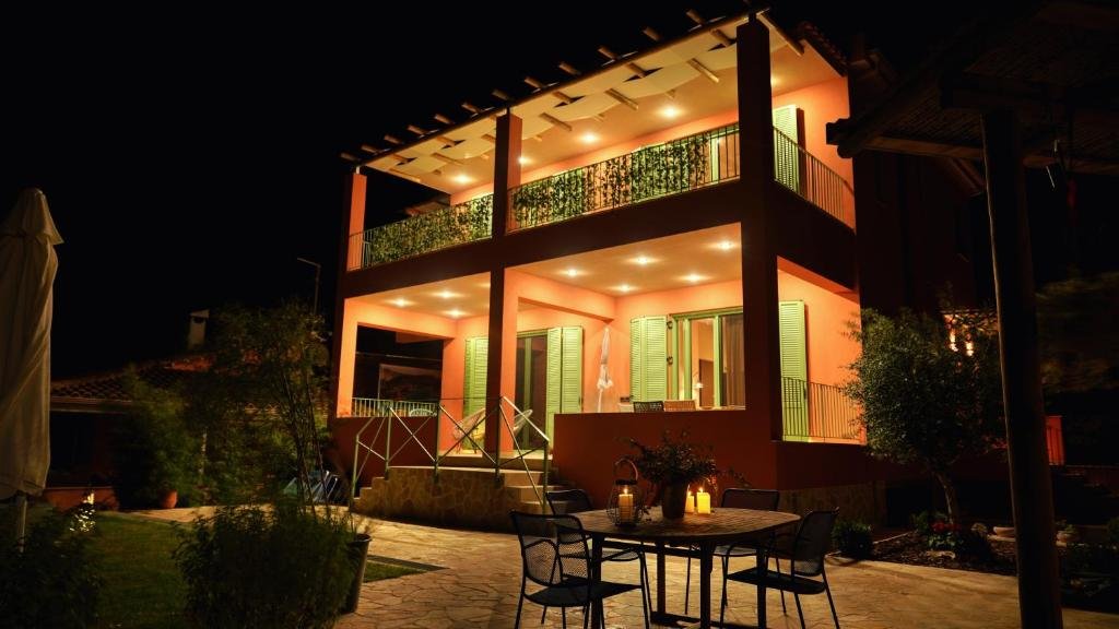 Alkyoni Luxury Apartments in Katakolon at night with warm lighting, balconies, and outdoor patio seating