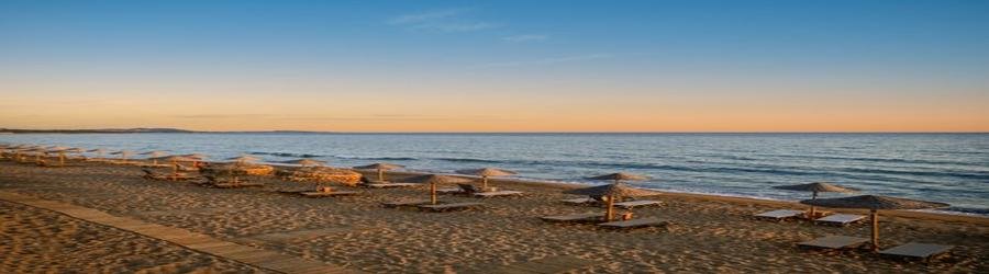 Kourouta Beach near Katakolon, Greece, with golden sand, calm blue sea, and rows of sunbeds at sunset.