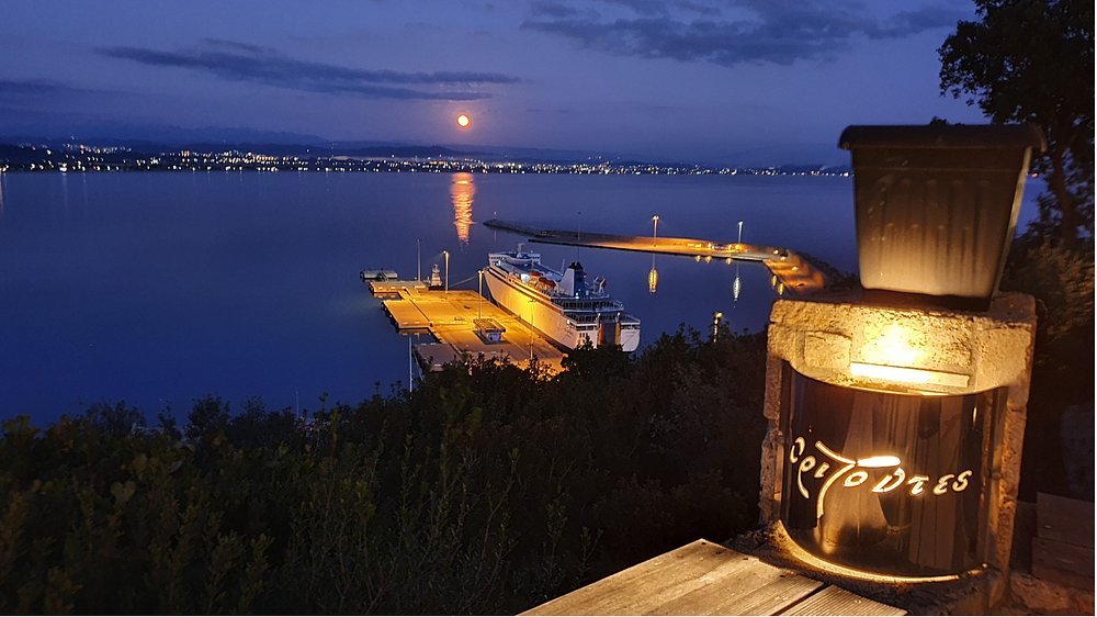 night view over Katakolon harbor with cruise ship, glowing lights, and moon reflection from Orizontes View Hotel
