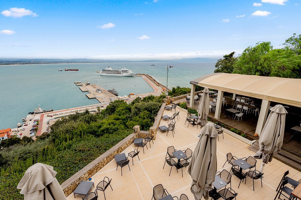 outdoor terrace dining area overlooking Katakolon port with sea views and seating at Orizontes View Hoteloverlooking a harbor and a docked cruise ship in the distance.