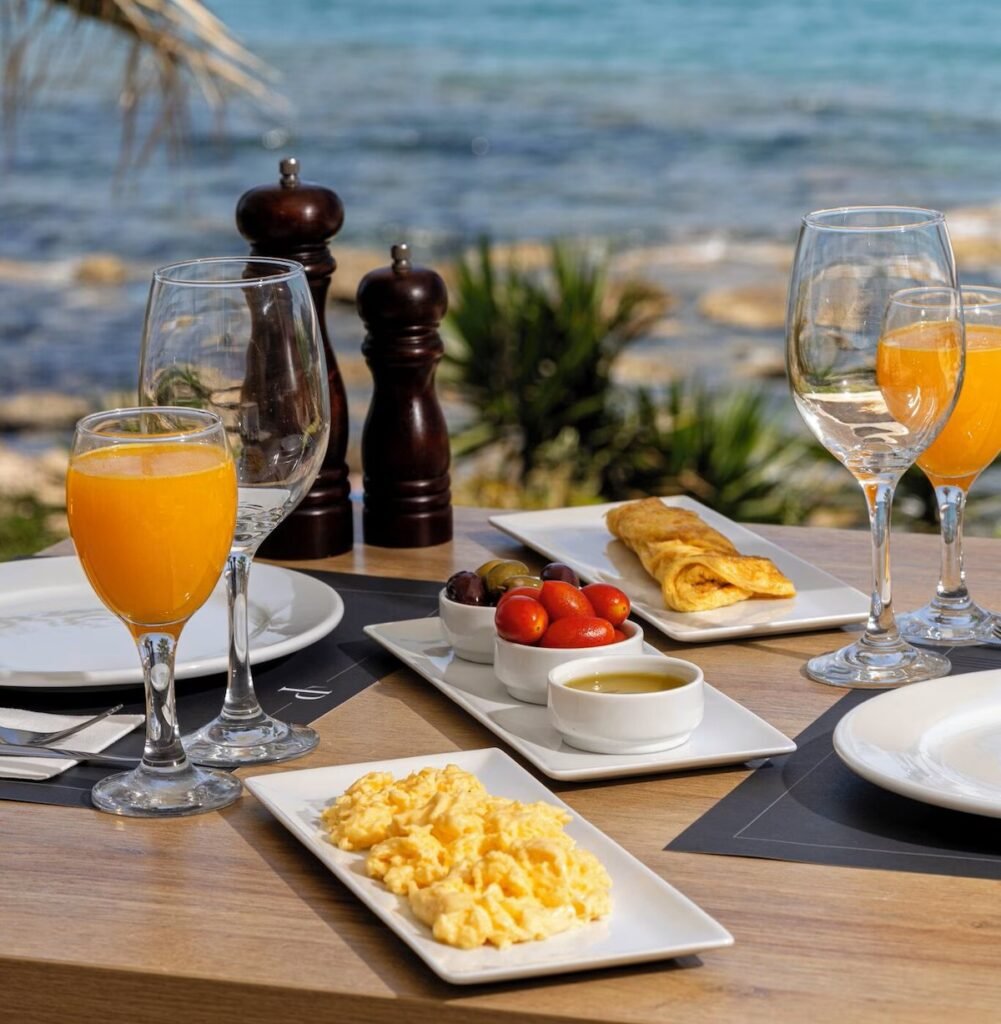 beachfront breakfast with orange juice, olives, eggs, and sea view at PHEIA Vriniotis Resorts