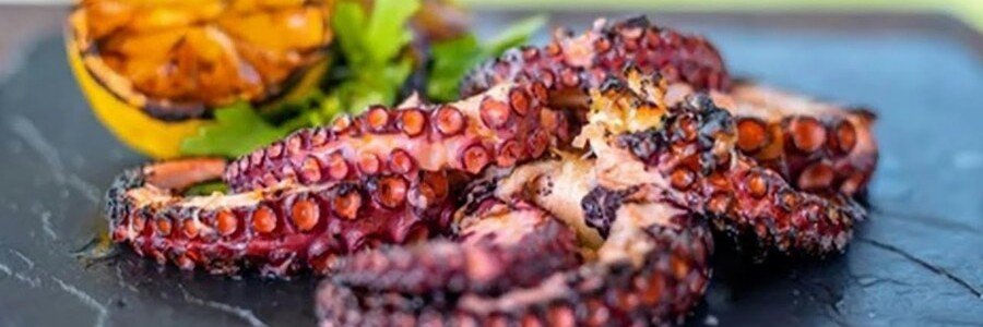 grilled octopus with charred edges served with lemon and herbs on a plate