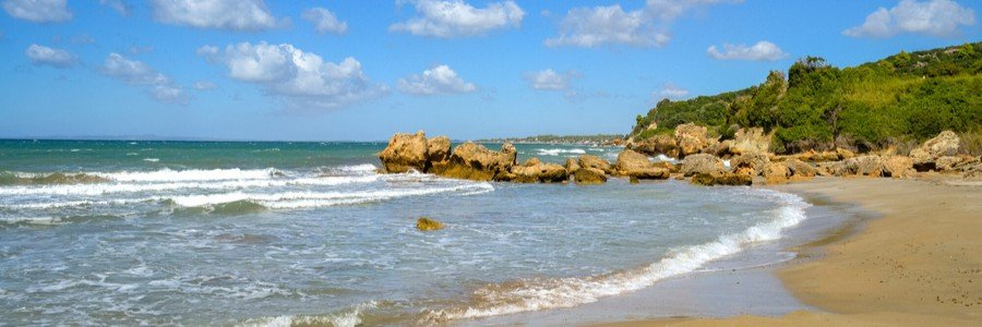Leventochori Beach with sandy shoreline, turquoise water, and rocky coastline under a blue sky