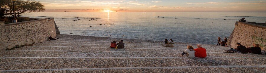 People sitting on stone steps along the Livorno seafront at sunset