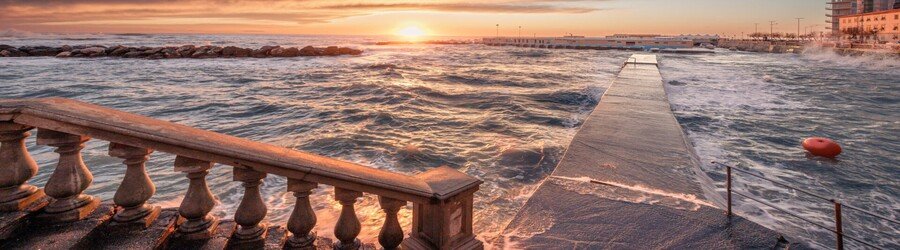 Lungomare seafront walkway in Livorno at sunset with waves and stone balustrade
