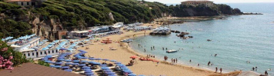 Quercetano Bay beach near Livorno with umbrellas, clear water, and rocky cove