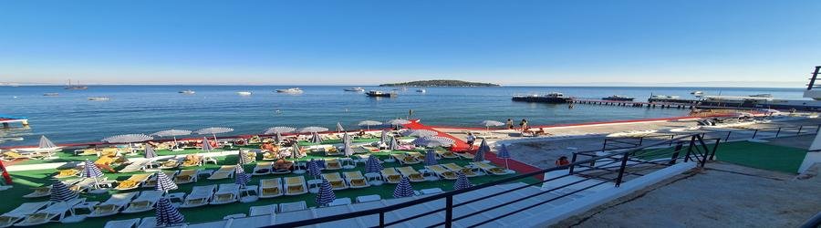 Buyukada Beach on the Princes’ Islands, featuring striped umbrellas, sunbeds, and boats anchored offshore in the sparkling blue sea.