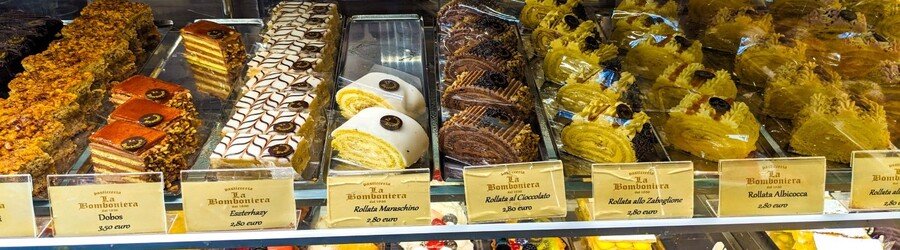 Display of traditional Trieste desserts in a pastry shop including layered cakes and rolled pastries
