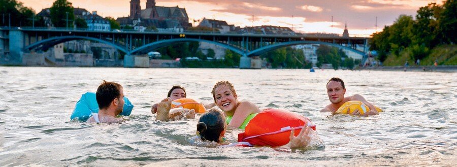 People floating in the Rhine River with colorful Wickelfisch swim bags in Basel Switzerland