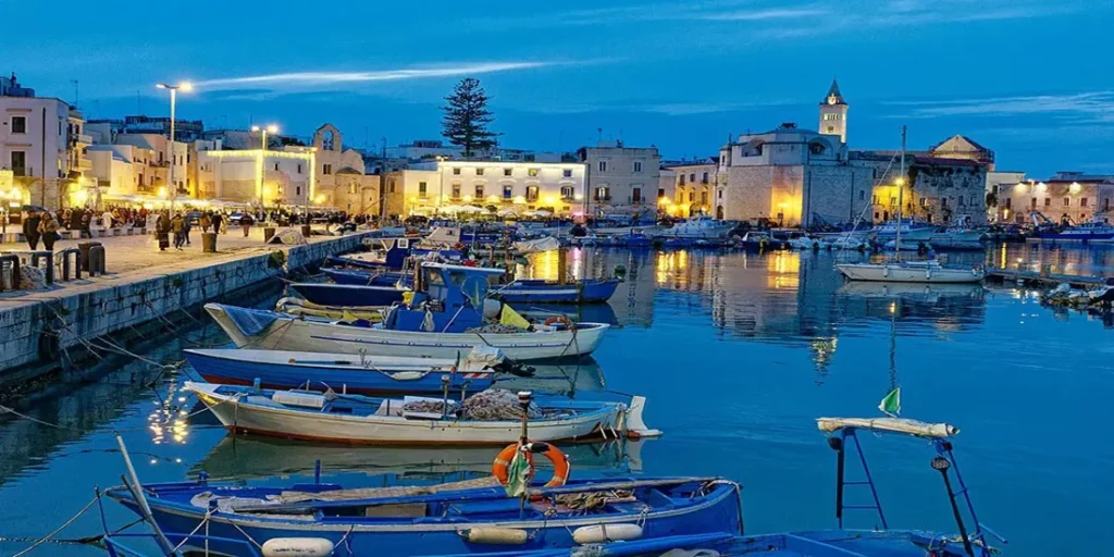 Evening view of Barletta’s harbor with fishing boats and historic buildings lit along the waterfront., Discover Beautiful Barletta on the Adriatic