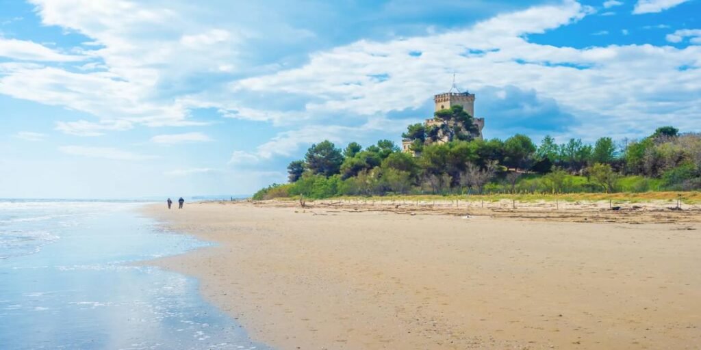 Beautiful Pescara Italy beach with golden sand, turquoise sea, and a historic stone tower surrounded by lush greenery.