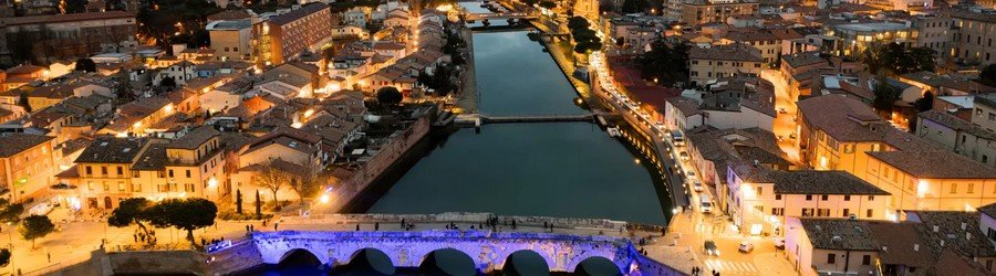 Rimini city at night along the river, also lit by historic bridges