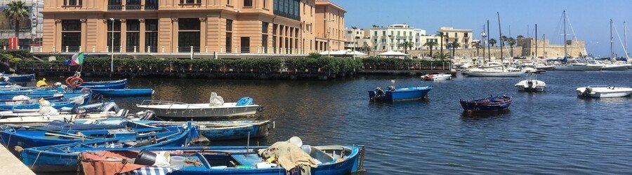 Small fishing boats in Bari harbor with historic waterfront buildings and marina