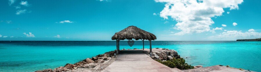 Thatched hut at the end of a seaside walkway overlooking bright turquoise Caribbean water in Curacao.