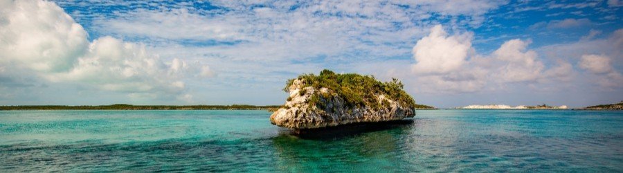 Small rocky island surrounded by clear turquoise water under a bright blue sky in the Exumas, Bahamas.