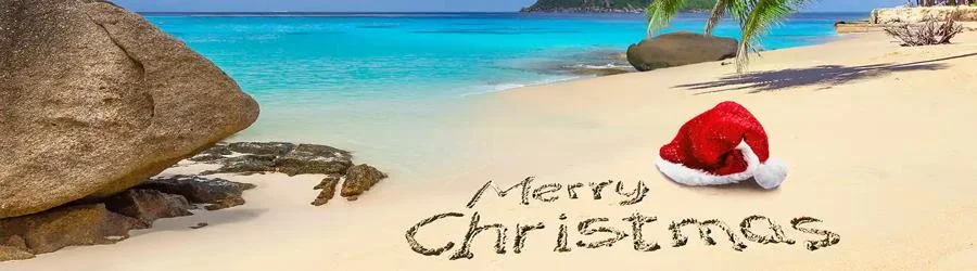 Tropical Christmas beach with a red Santa hat, Merry Christmas written in golden sand, turquoise ocean waves, palm trees, and colorful hibiscus flowers.