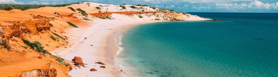 A sweeping view of sandy dunes and calm turquoise water stretching along Western Australia’s remote northern coastline.