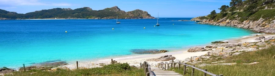 Boardwalk leading to a turquoise cove on the Cíes Islands in Galicia, Spain.
