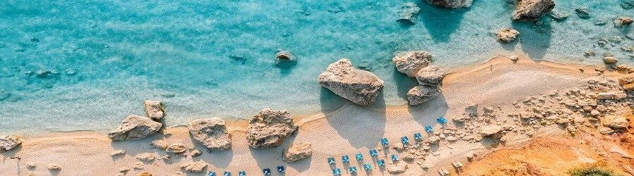 Aerial view of a rocky beach in Antipaxos with clear turquoise water and rows of blue sunbeds along the shoreline.