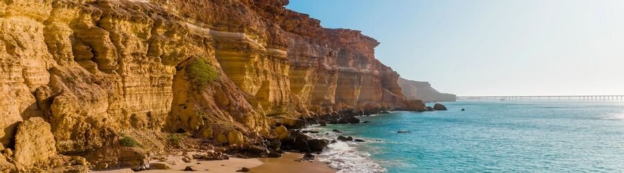 Towering red sandstone cliffs rising above a quiet beach with clear blue water in Kalbarri’s Lucky Bay.