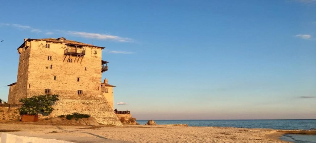 Golden sands and turquoise waters along the Beaches of Ouranoupoli in Greece, framed by a historic stone tower.