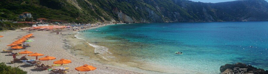 Clear turquoise water and sunbeds with orange umbrellas at Paralia Petani Beach on Kefalonia’s Paliki peninsula.