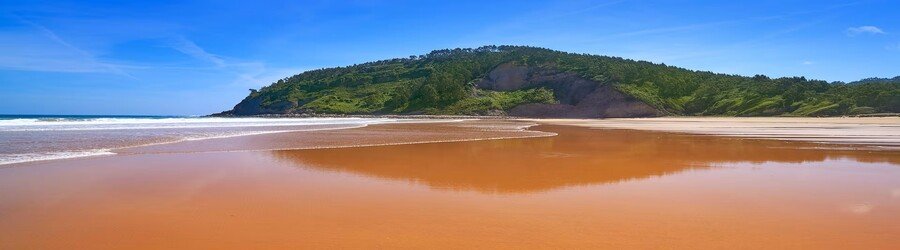 Wide sandy beach with shallow reflections and green cliffs on Spain’s northern coast.