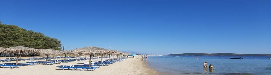 Xiropotamos Beach in Ouranoupoli, Greece with sunbeds, straw umbrellas, and calm shallow waters.