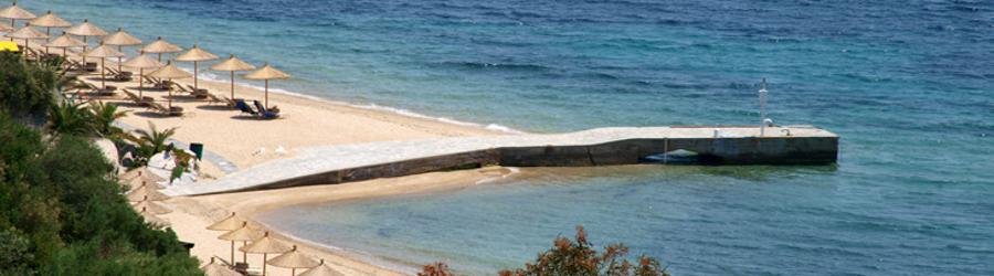 Ouranoupoli Beach in Greece with golden sand, clear blue water, and sun loungers shaded by straw umbrellas.