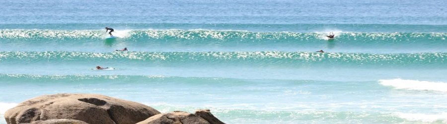 Surfers riding perfect rolling waves under the bright sun along Galicia’s Atlantic coastline.