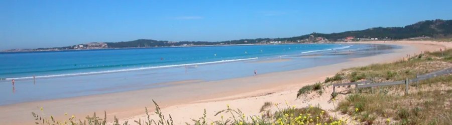 Wide sandy beach with calm turquoise water and distant coastal hills on a sunny day in Galicia, Spain.