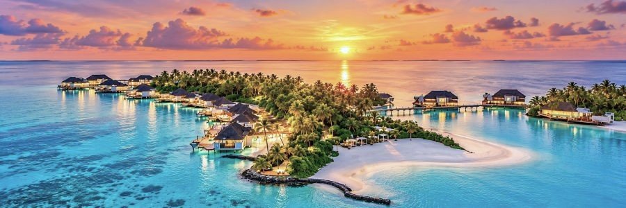 Cheval Blanc Randheli in the Maldives surrounded by turquoise water, white sand beaches, palm trees, and overwater villas at sunset.