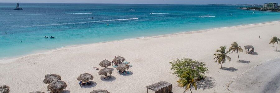 10 Most Beautiful Beaches | Eagle Beach, Aruba Eagle Beach in Aruba with wide white sand, turquoise Caribbean water, palm trees, palapas, and a sailboat offshore.