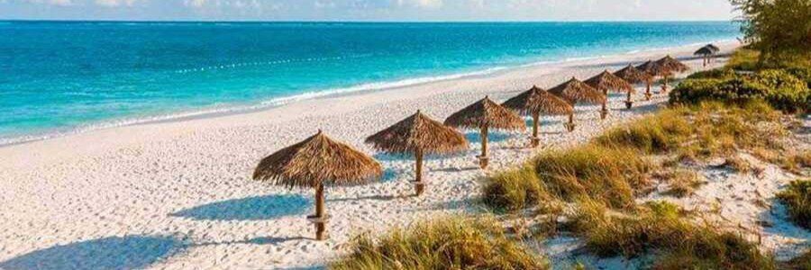10 Most Beautiful Beaches | Grace Bay Beach Grace Bay Beach in Turks and Caicos with white sand, clear turquoise water, beach umbrellas, and coastal grass.