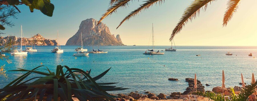 Ibiza coastline with Es Vedra rock island clear Mediterranean water boats and sunset sky