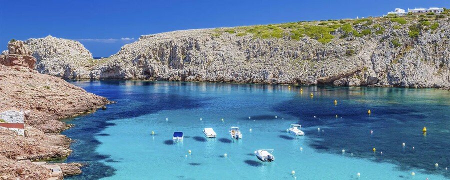 Turquoise cala bay in Menorca with clear Mediterranean water boats and rocky coastal cliffs