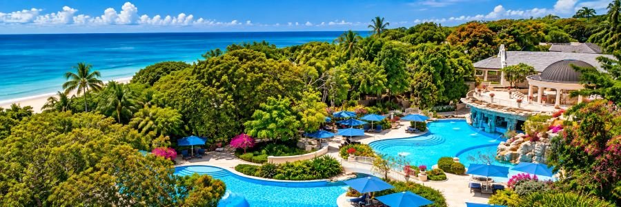 Sandy Lane in Barbados with a tropical swimming pool, lush gardens, palm trees, and beautiful Caribbean Sea views.