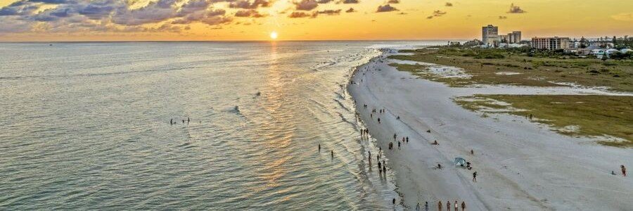 10 Most Beautiful Beaches | Siesta Beach Siesta Beach in Sarasota, Florida, with a wide white shoreline, calm Gulf water, beachgoers, and a golden sunset.