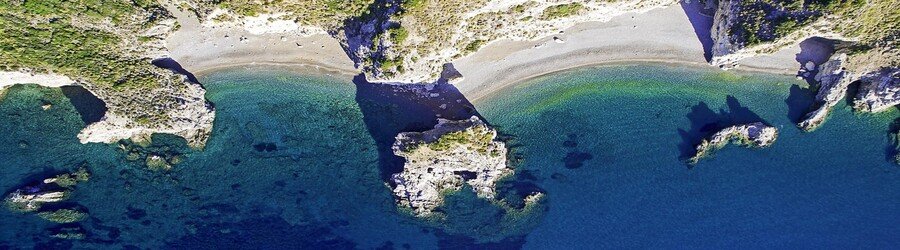 Aerial view of Kaladi Beach in Kythira featuring a curved shoreline, deep blue water, and dramatic rock formations.