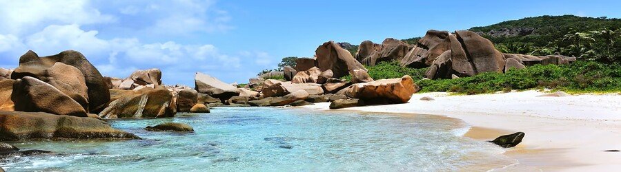 White sand beach in the Seychelles with clear turquoise water and large granite boulders along the shoreline