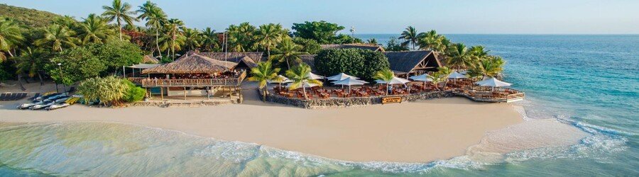 White sand beach in Fiji with palm trees, beachfront resort, and clear blue ocean water
