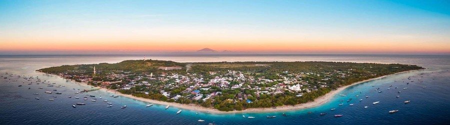 Aerial view of Gili Trawangan at sunrise with boats anchored along its turquoise shoreline.