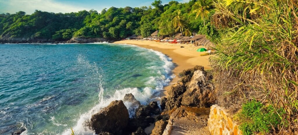 Golden sunset over a secluded Oaxaca beach with waves washing ashore and lush tropical hills. Beaches of Oaxaca