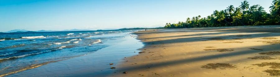 Mission Beach in Queensland with palm trees, golden sand, and gentle ocean waves at sunset.
