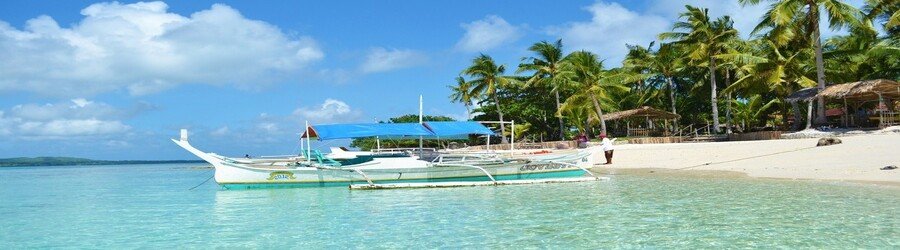 Traditional boat anchored in shallow turquoise water along a palm-lined beach on Bantayan Isla