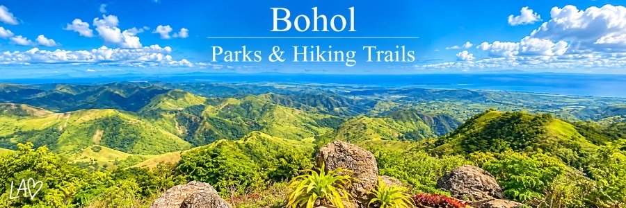 Panoramic view of Bohol's lush green mountains, rolling hills, and rocky highland scenery beneath a brilliant blue sky with scattered white clouds.