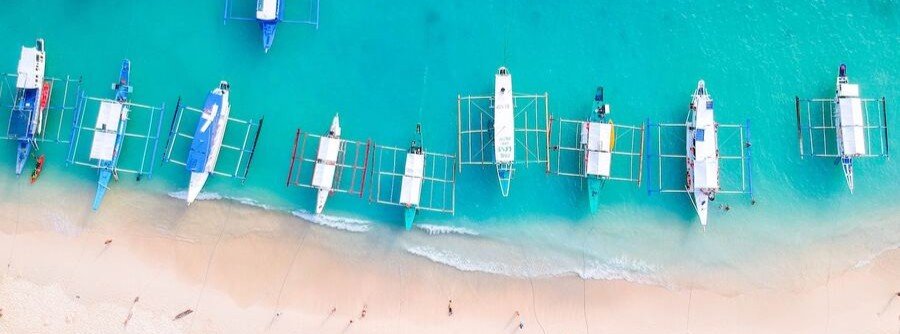 traditional outrigger boats lined along a turquoise beach in Luzon Philippines